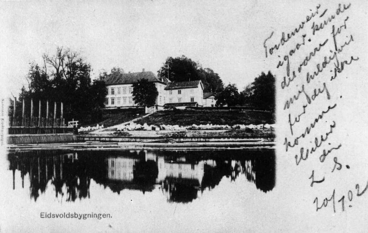 Eidsvollsbygningen, Eidsvoll, Akershus. Fotografi av postkort datert 20/7 1902. Bygningen sett fra elva. påskrevet hilsen.