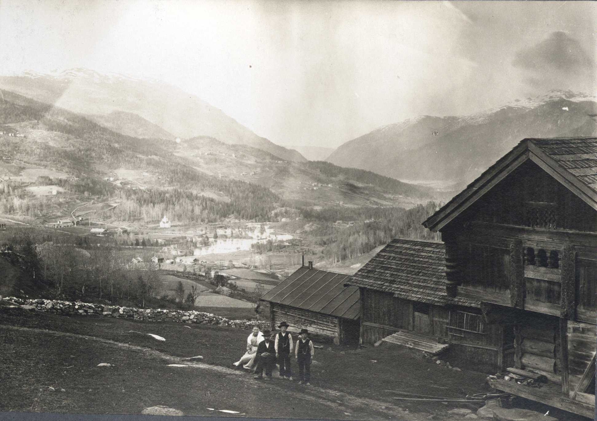 Gårdstun, Øvre Åbø , Hjartdal, Telemark. Fotografert 1915. Familie stående foran stabbur med landskap i bakgrunn.