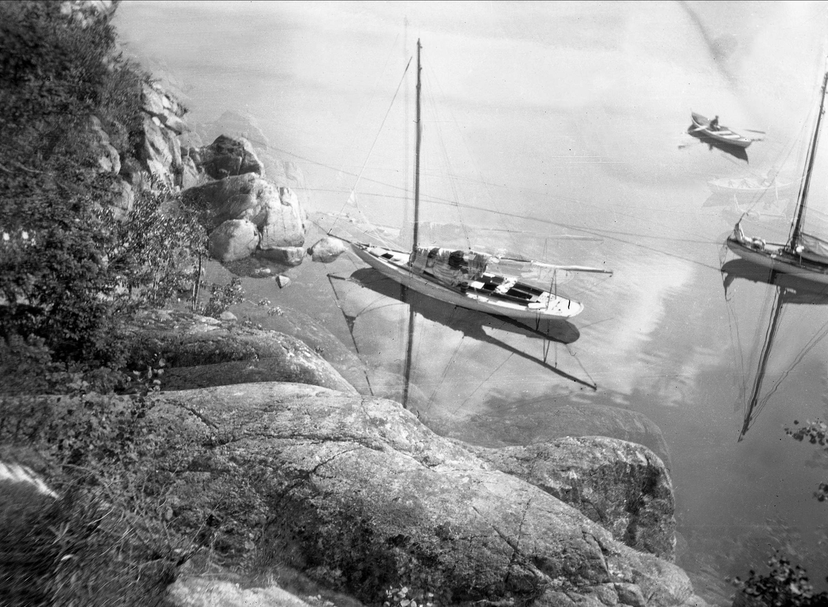To seilbåter og en person i robåt sett fra et svarberg. Robsahm og Lund.
