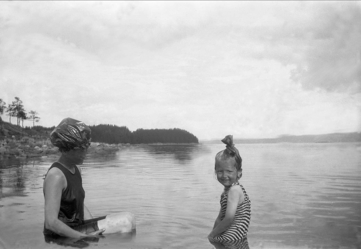 En kvinne og en jente kledd med badedrakt bader i et vann. Robsahm og Lund.
