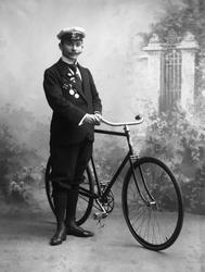 Portrett, mann med uniformslue, medaljer og sykkel.