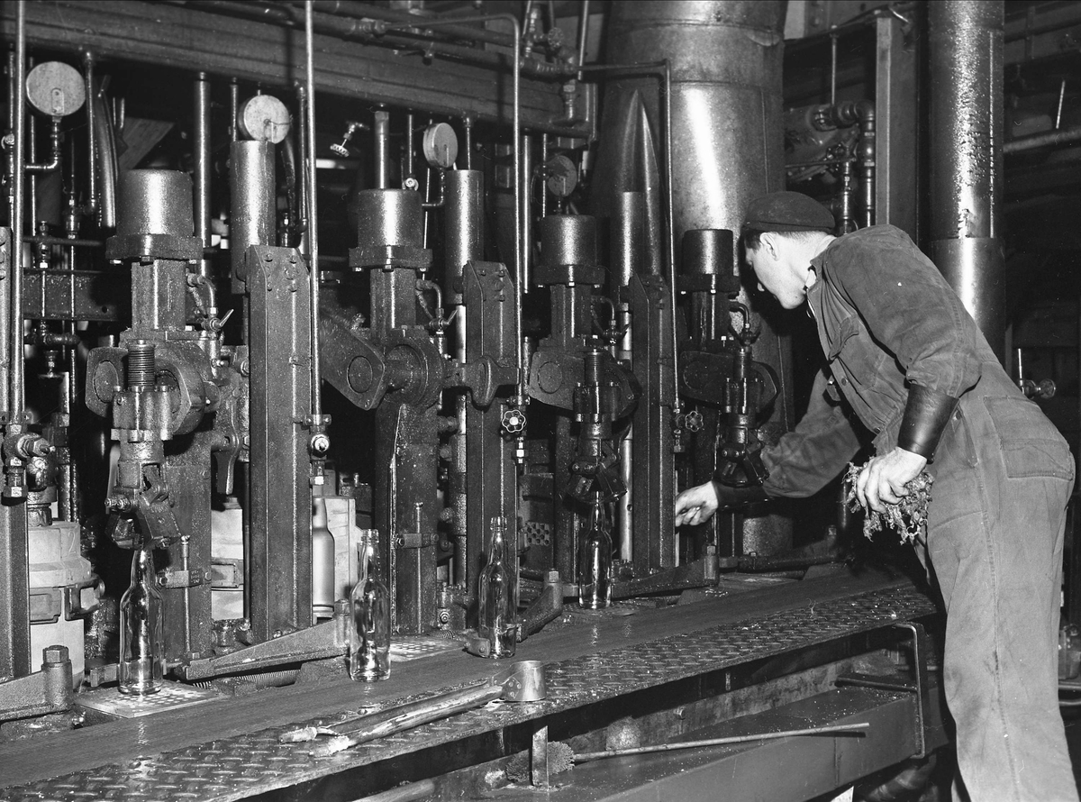 Moss Glassverk (1898-1999), 15.01.1957. Mann ved maskin. Produksjon av flasker.
 