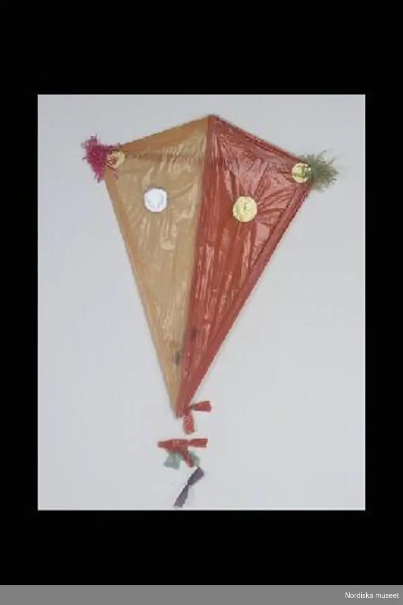 Inventering Sesam 1996-1999:
L  70   B  55 (cm)
Drake, leksak, stomme av trä klädd med orange och rött papper med påklistrade runda prickar av glanspapper i guld och silver, papperstofsar i rött och  grönt, svans av snöre med rosetter i rött, grönt, blått och gult. Påklistrad prislapp: "2.00".
Anna Womack mars 1998