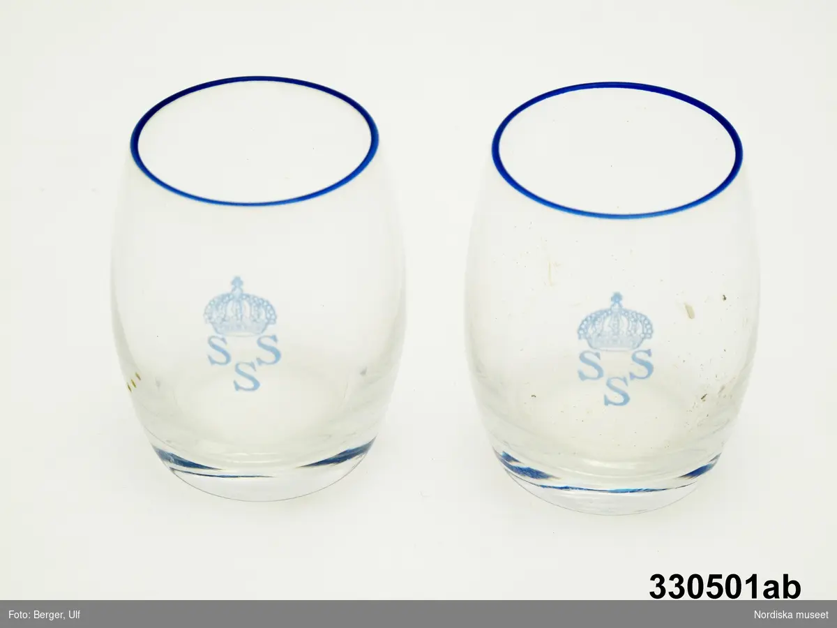 Nubbeglas, 2 st,  tunt klarglas, svagt bukig form. Dekor av en blå smal kantrand samt Stockholms Seglar Sällskaps emblem (SSS samt en kungakrona).
/Cecilia Wallquist och Kersti Wikström 2010-12-16.