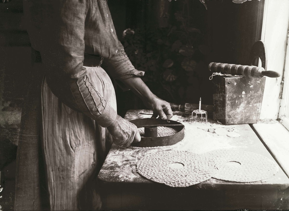 Knäckebrödsbakning. Kvinna stansar hål ur degen med ett brödmått. Bjurbäcken, Manskogs socken, Värmland.