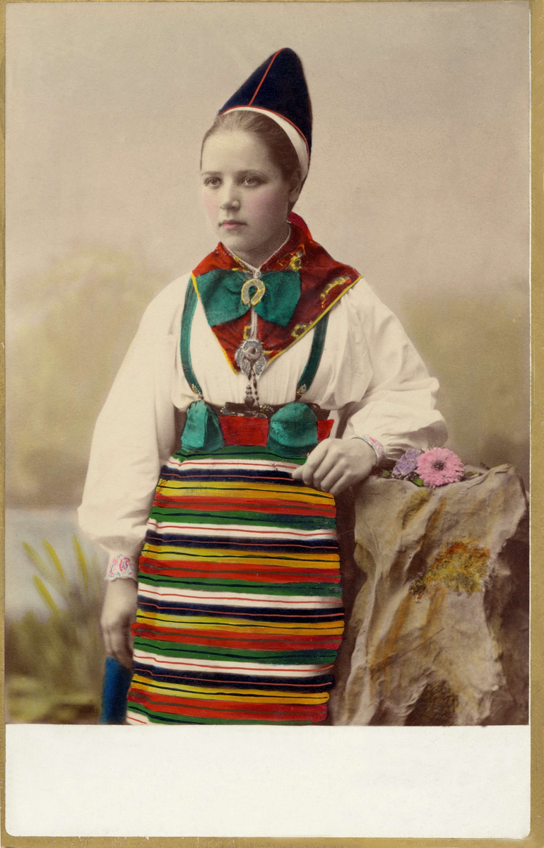 Ateljéporträtt av Eskils Greta Olsdotter, Lerdal, klädd i folkdräkt från Rättvik i dalarna. Kolorerat fotografi.