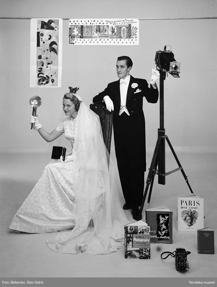 Bröllopsfoto av fotograf  Hans Hammarskiöld och hans hustru - omgivna av attribut som visar deras intresseområden fotografi och konst.