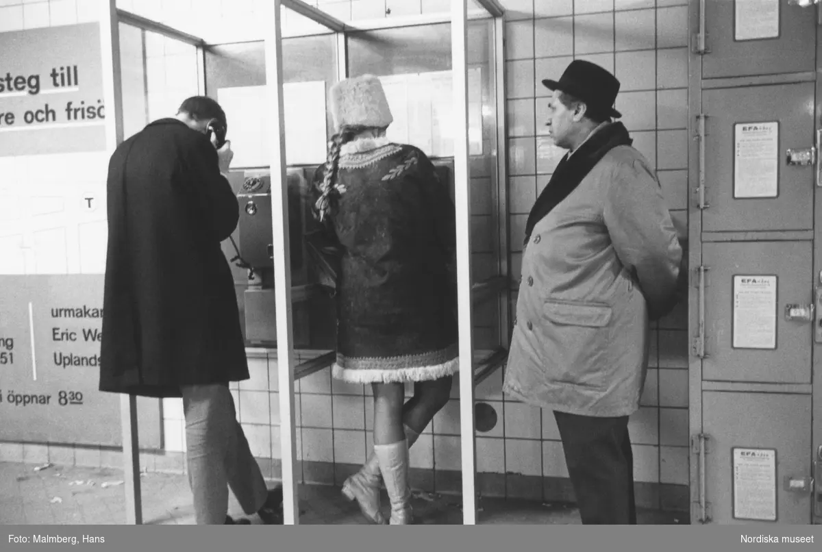 Stockholm 1968. 
Ung kvinna i telefonkiosk, köande man.