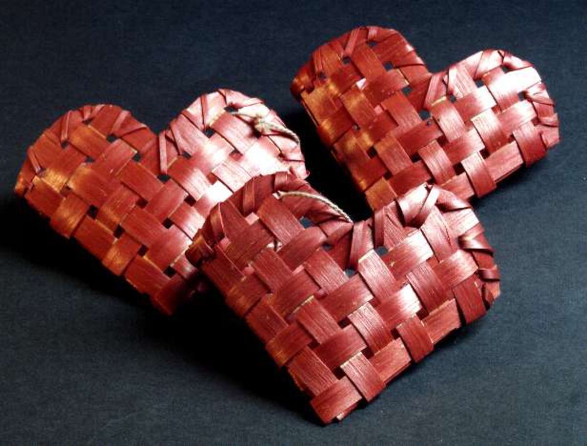 Tre korgar att hänga i julgran, av flätad, rödlackerad näver, i form av hjärtan. Rosa bomullssnodd.
