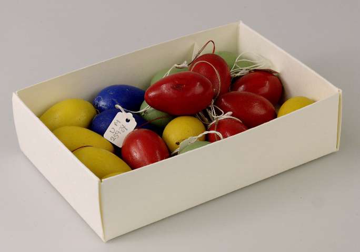 18 små ägg av trä målade i olika färger; gult, rött, blått och grönt med en liten trådögla för upphängning i påskris. Förvaras i pappask med påskrift: PÅSK.

