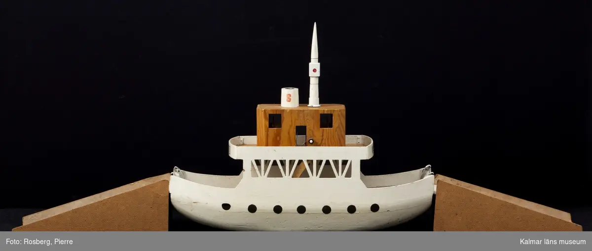 KLM 44679. Båt. Leksaksbåt, färja med två påfartsramper. Av trä.  Själva färjan vitmålad. Ramperna omålade. Båten är en modell av en Ölandsfärja, Kalmar II. Tillverkad av givarens morfar Thure Karlsson, Ljungsbro.