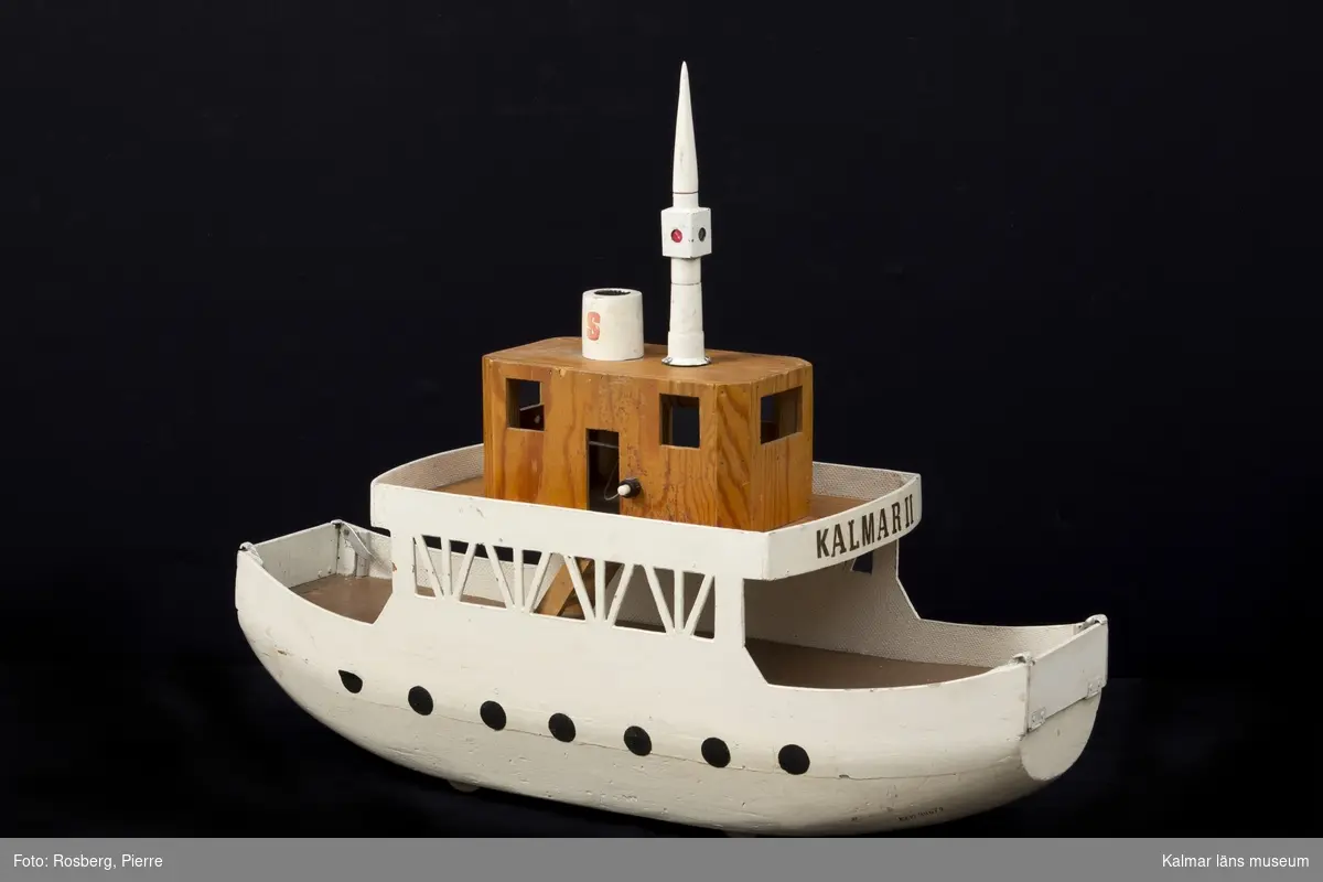 KLM 44679. Båt. Leksaksbåt, färja med två påfartsramper. Av trä.  Själva färjan vitmålad. Ramperna omålade. Båten är en modell av en Ölandsfärja, Kalmar II. Tillverkad av givarens morfar Thure Karlsson, Ljungsbro.