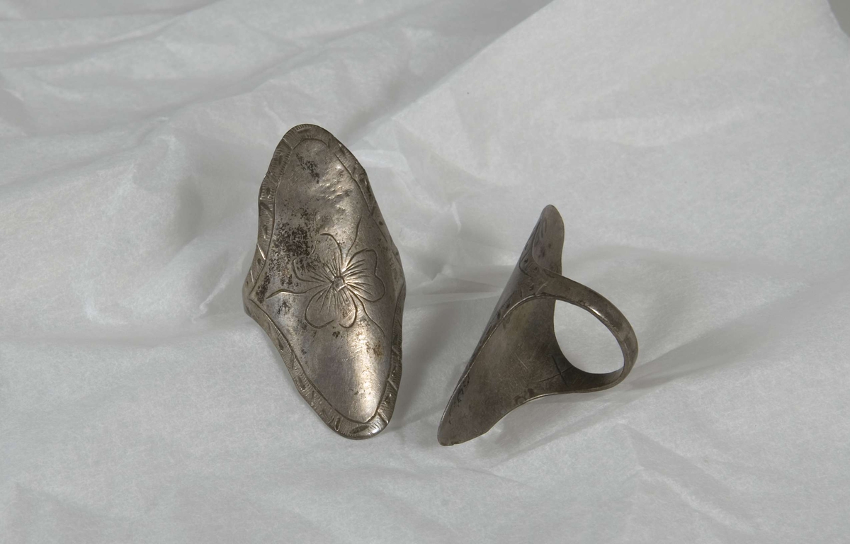 Två ringar av silver, med ovala plattor. Plattorna är graverade, en smal kantdekor och en blomma.  Märkta B.979. 
