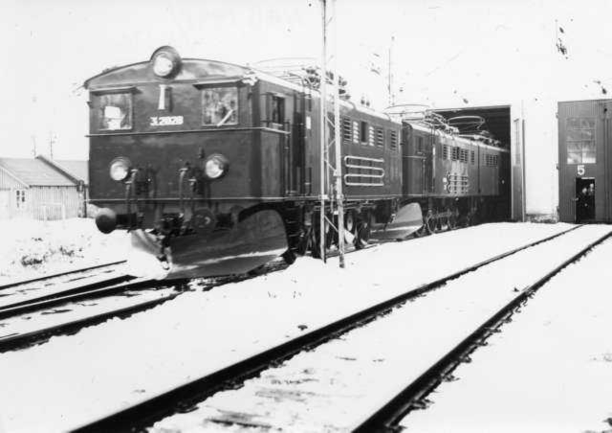 Elektrisk lokomotiv delvis inne i en lokstall. Verkstedtomta Narvik Ombygd  El.3 lok til treseksjons-lok. Ombygningen skjedde i NSB`s verksted i Narvik, Ofotbanen. 
 Det första sammankopplade loket med tre sektioner gjordes på försök 1951 med Of3 56-72-73 som återställdes 1952 till två sektioner. 1953 började man på allvar bygga om först Of3 65-66-67 till tre sektioner. Sedan 1954 och 1955 blev fler ombyggd. Är helt säker på att ingen El3 byggdes om till tre sektioner före 1953. Mer troligt är första år 1954. Alltså bör bilden vara från tidigaste år 1953.