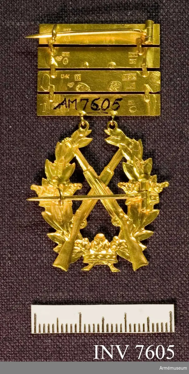 Ett guldmärke med fyra guldplattor som vardera har präglingen 1910, 1911, 1912, 1913. Märket förvaras i en gul ask med locket täckt av en vit etikett med text: Årtalsmärke af guld.