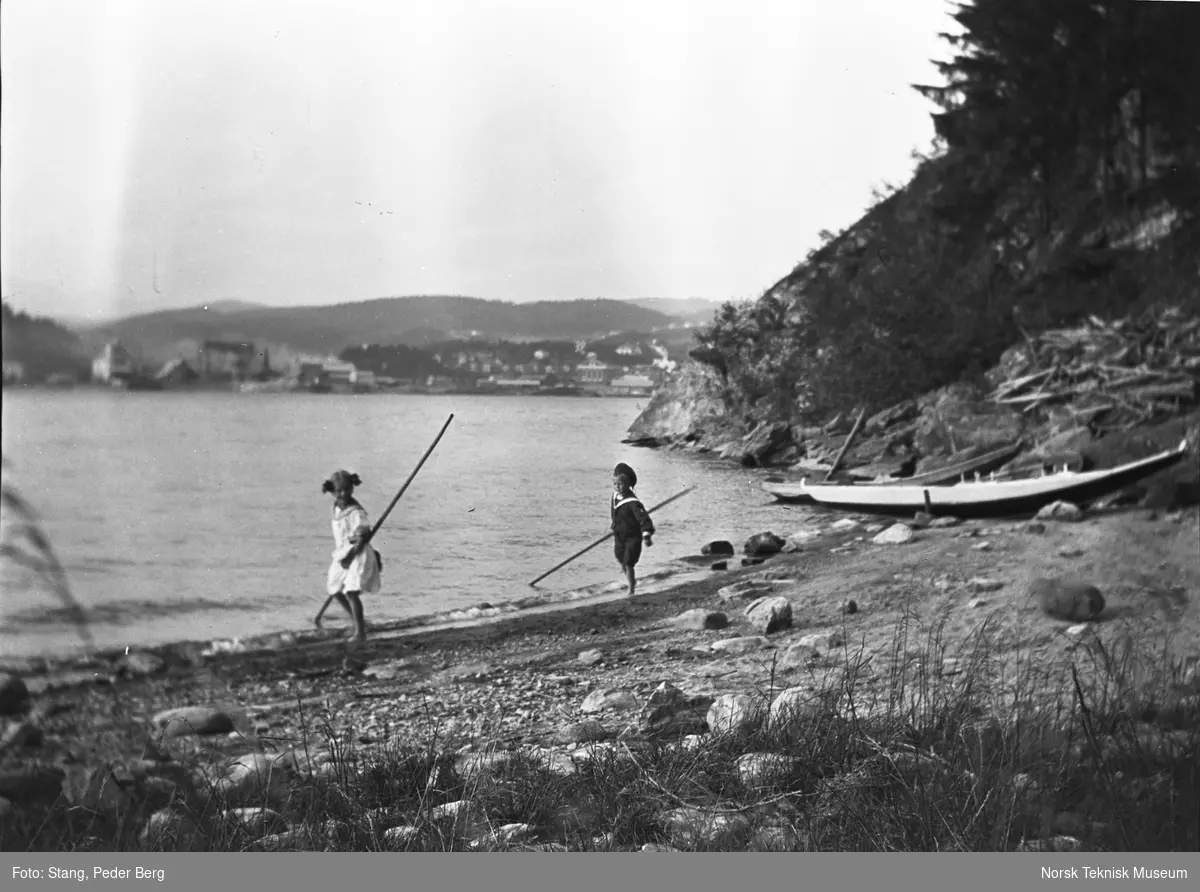 To barn leker i vannkanten, i bakgrunnen ses industribyen Notodden