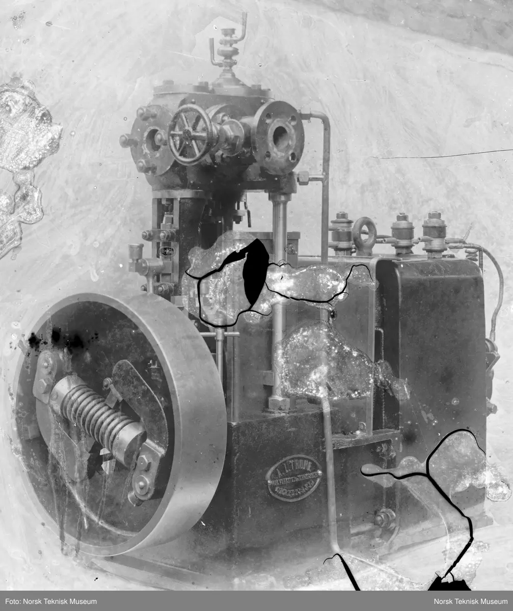 Dampmaskin merket A.L. Thune Mek. Verksted & Jernstøberi Kristiania, laget på Thunes Mekaniske Verksted på Skøyen i Oslo. Resten av bakgrunn dekket over med tusj.