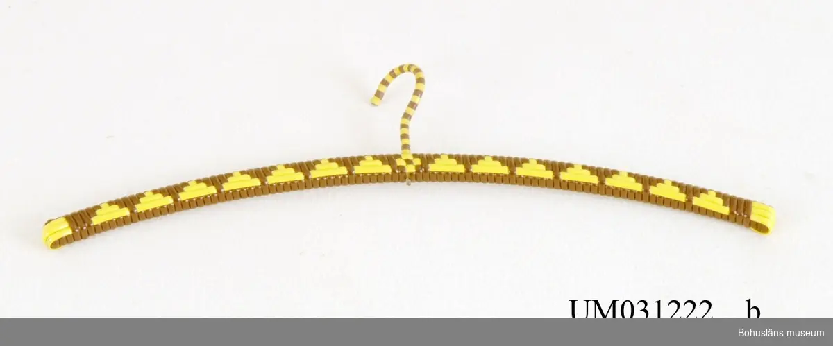 Plastklädd smal trägalge lindad med kraftig gul och brun  plastrem i dekorativt mönster, UM031222:1 och UM031222:2. 1970-tal.