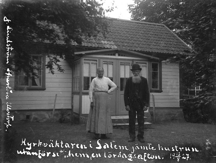 Enligt text på fotot: "Kyrkväktaren i Salem jämte hustrun utanför sitt hem, en lördagsafton. 13/8 1927. Lindström, Sparlösa Ulvstorp".