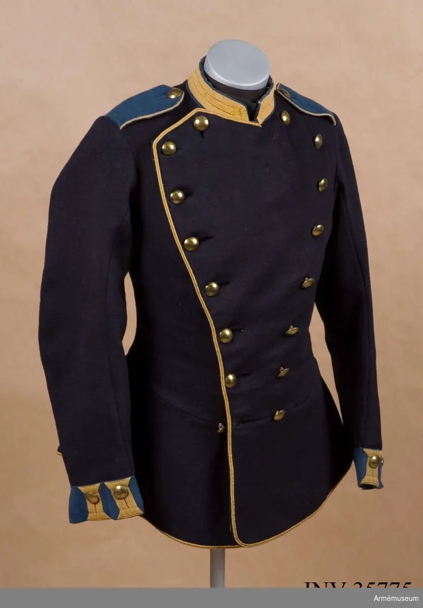 Grupp C I.
Vapenrock av mörkblått kläde med ljustblå detaljer samt gult ullgarnsband för distinktionskorpral.
