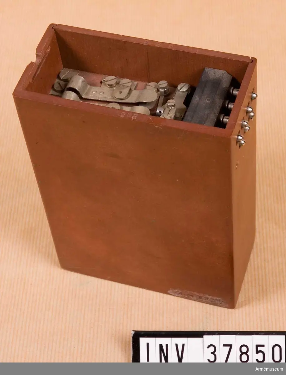 Grupp H I. 
Fälttelefonapparat m/1909 med 7-delig propp.
Fiberlåda med innehåll. Utan hörnbeslag. Saknas: lådans lock med tillhöriga delar.