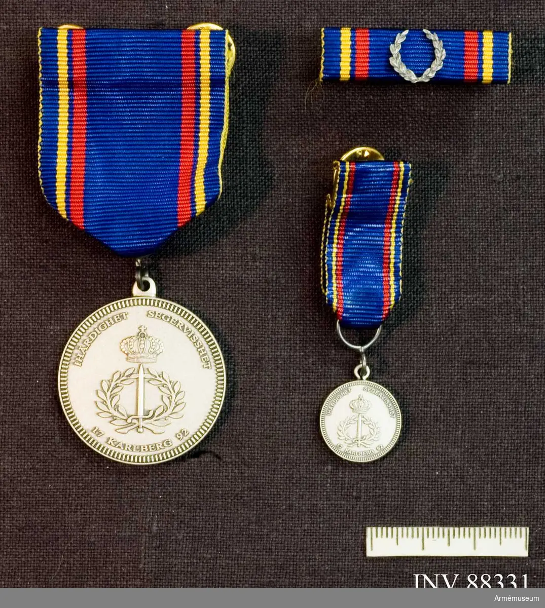 Tre samhörande föremål; en medalj, en minatyrmedalj och ett släpspänne. Bandet blått med en gul och en röd rand på vardera sidan..