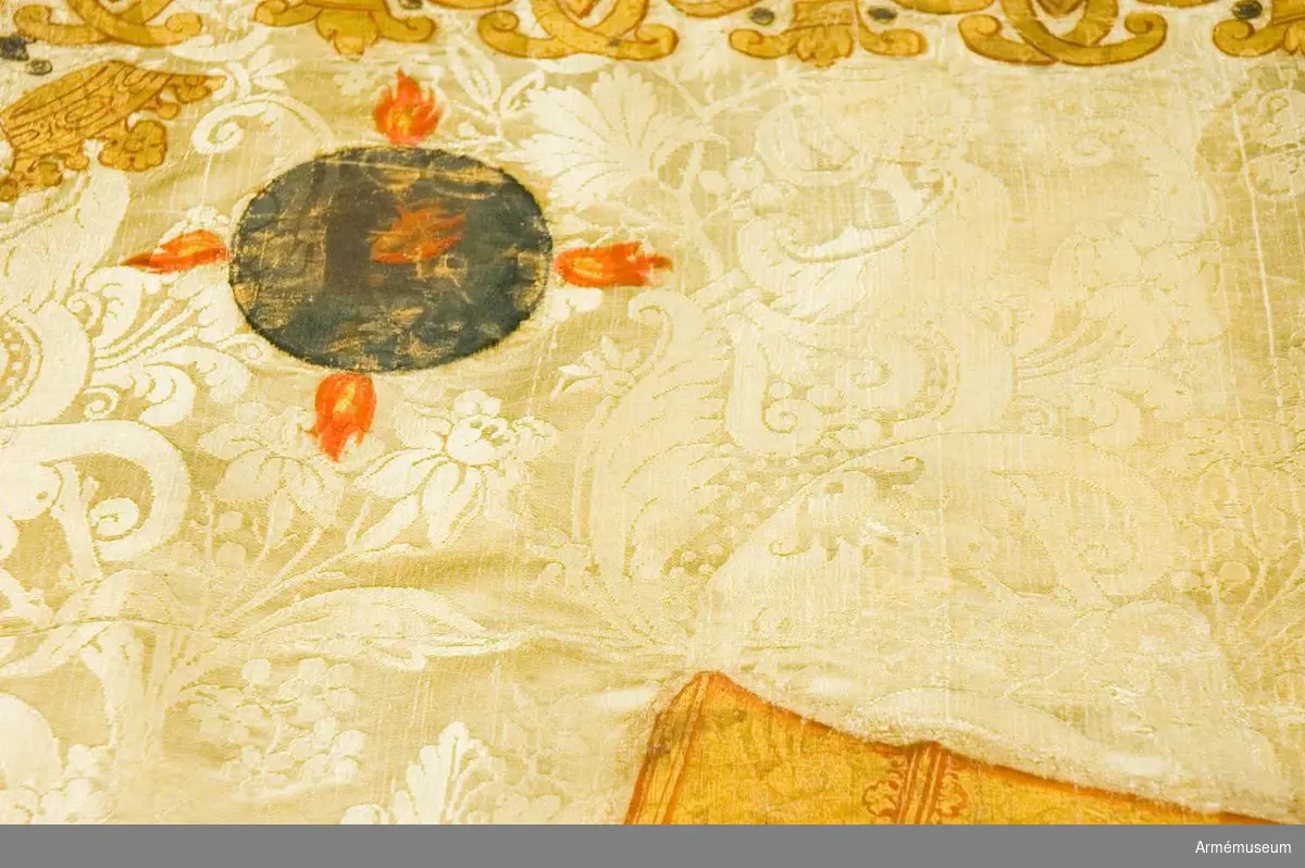 Grupp B.
Pukfana, märkt 1716. Duk av sidendamast, vit, uppfodrad på ylle, med målade emblem i guld, rött, blått och brunt. I mitten Karl XII:s krönta namnchiffer mellan årtalet 17 - 16, därunder korslagda  palmkvistar och kanoner med Karl XII:s namnchiffer. I hörnen  fyrkulor blå och silver med röda flammor. Runt fanan en bård, korslagda palmkvistar bildar en del av mönstret.

Fodret lossat och har eget nummer. (AM