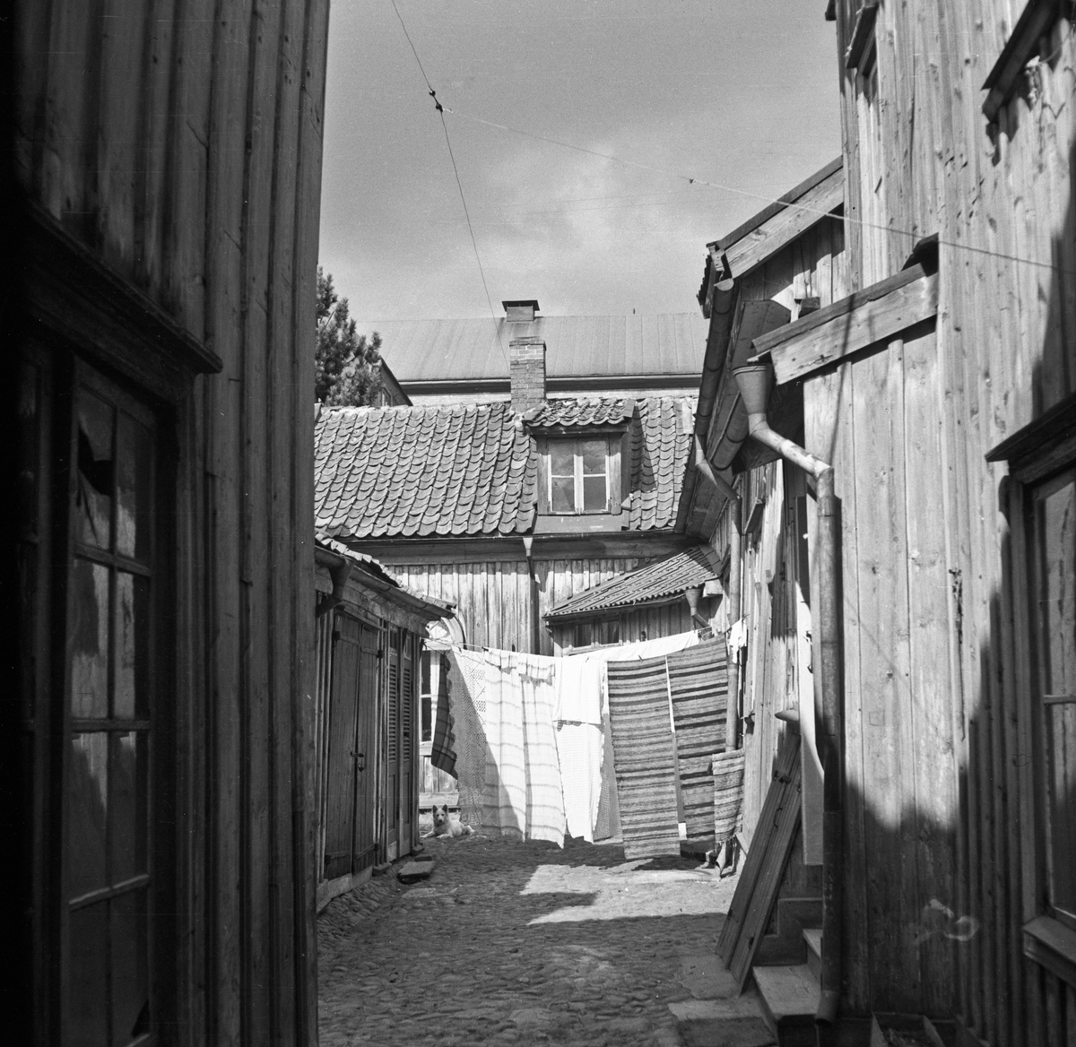 Bakgård i Jönköping belagd med kullersten. Mattor hänger på tork mellan husen.