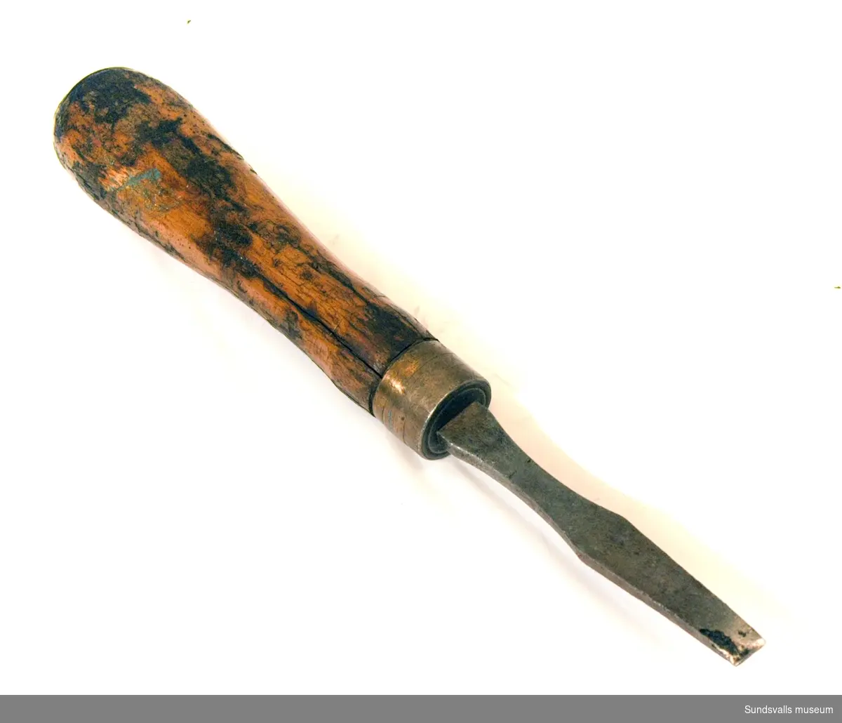 Verktyg med trähandtag. Smitt järn i mejselliknande form tillverkad hos C.W. Jansson i Torshälla. Märkt '12'. Användes på Wiiforsens Kraftstation.