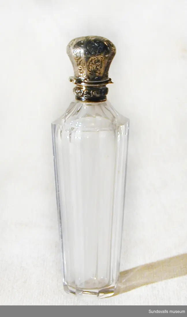 Parfymflaska tillverkad i glas med en mönstrad kork av nysilver.