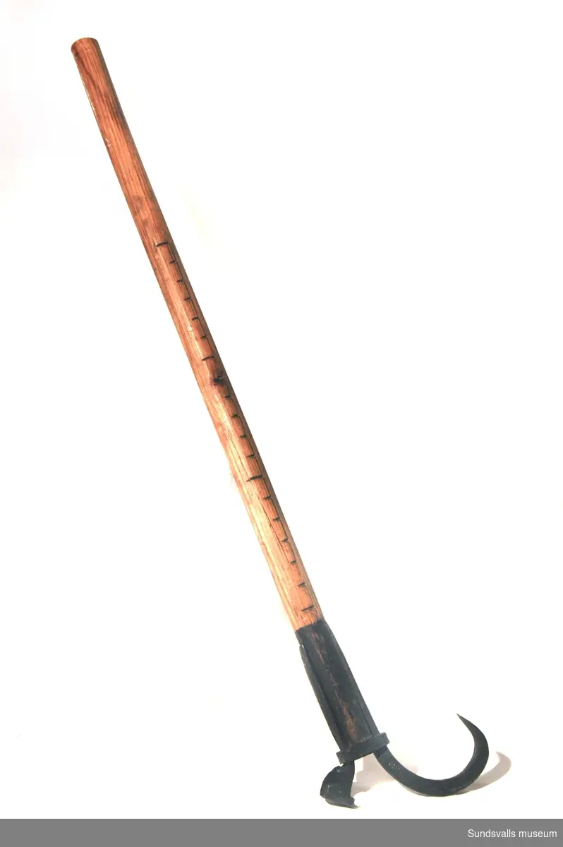 Redskap med två järnkrokar framtill, en spetsig och en mindre, bred och platt, vilka är fästade på ett träskaft med hjälp av skruvar och en järnring. På skaftet är en graderad skala inskuren. Den platta kroken är märkt 'PATENT'.