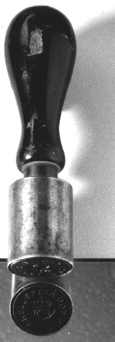 Sigillstamp av stål med text enligt signering/märkning.
Stampen försedd med päronformat svart skaft av trä. Längst ner mot
stampen sitter en mässingsgördel.