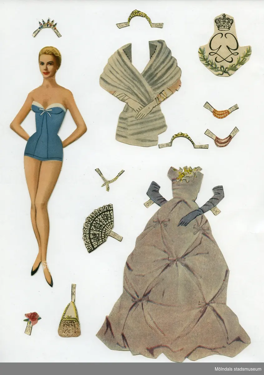 Klippdocka med kläder och tillbehör från 1950-talet. Docka och kläder märkta "Grace Kelly" - dockans namn.Dockan, av papp, föreställer filmstjärnan Grace Kelly, senare furstinna av Monaco (1929-1982), tryckt med fotolikhet. Hon är iklädd underkläder av baddräktsmodell, samt skor. Garderoben, urklippt ur tidning, består av sex blusar, en kjol, en dräkt med blus och kjol, kappa, fem aftonklänningar, fyra galaklänningar, brudklänning, samt minkstolor. Dockan har dessutom tillbehör som tio hattar, sex väskor, halsband, scarves, solfjädrar, toilet-artiklar, paraply, tiara och blommor. Flera av objekten finns i två eller tre exemplar. De mindre föremålen förvaras i ett valsedelkuvert. På kuvertet står skrivet "Småsaker, Grace Kelly, Pappersdocka", samt ett påklistrat monarkemblem.