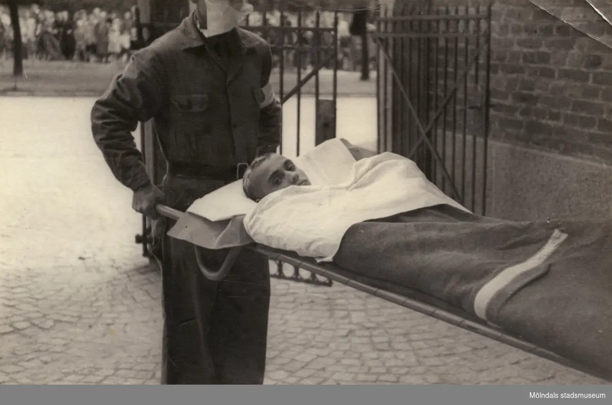 "Karantänsförläggning" på Kvarnbyskolan för överlevande från koncentrationsläger i Tyskland och Polen 1945.  
Skolan fungerade under denna sommar som beredsskapssjukhus.

En ung flykting på bår, buren av Röda Korsets personal.