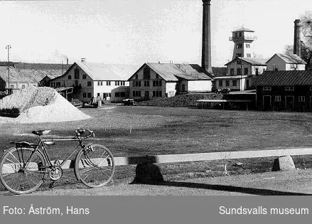 Svartvik på 1930-talet. Norra sågen med hyvleriet, pannhuset och vattentornet. Cykel med väska för reparation på ramenVykort utgivet av Föreningen Svartviksdagarna