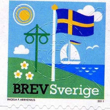 En midsommarstång bredvid en flaggstång med den svenska flaggan och ett hav med en segelbåt.