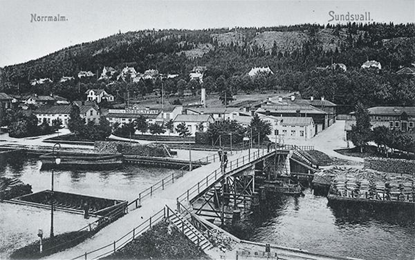 Gamla gångbron (kallad Puckelbron samt Kamelryggen) som förband Norrmalm  med Stenstaden (låg i förlängningen av Norrlandsgatan). Bron raserades vid  översvämningen våren 1919 och byggdes inte upp igen. Vykort. - Sundsvalls  museum / DigitaltMuseum