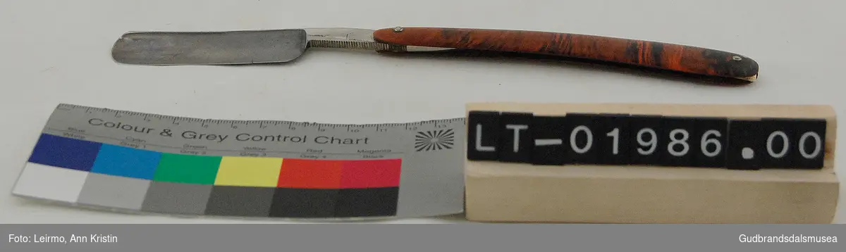 Sammenleggbar barberkniv, med svart og brunt skaft, har tilhørende etui.