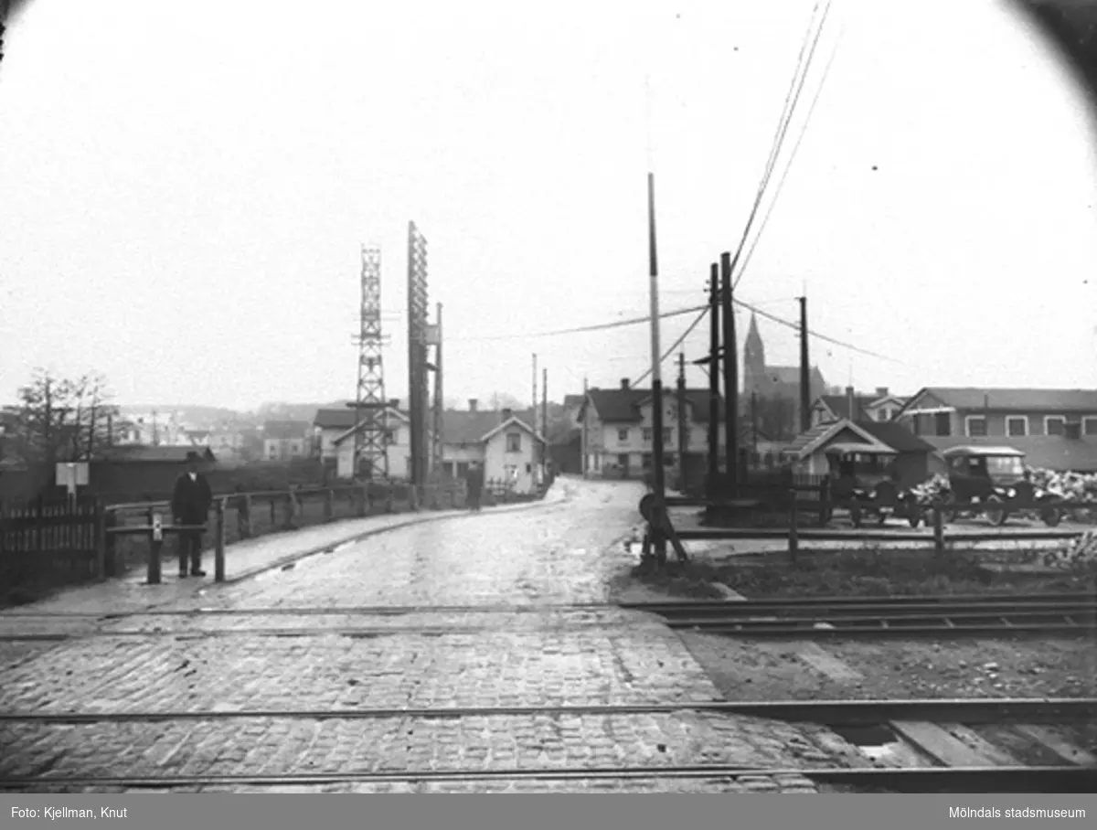 Järnvägsövergången vid Mölndals nedre, 1920-tal. Fotografen har stått på Kvarnbygatan strax öster om järnvägsspåren och fotat mot väster. 
I bakgrunden ses Kungsbackavägen 1 samt Göteborgsvägen 1 och 3 och framför spårvagnshallarna.
