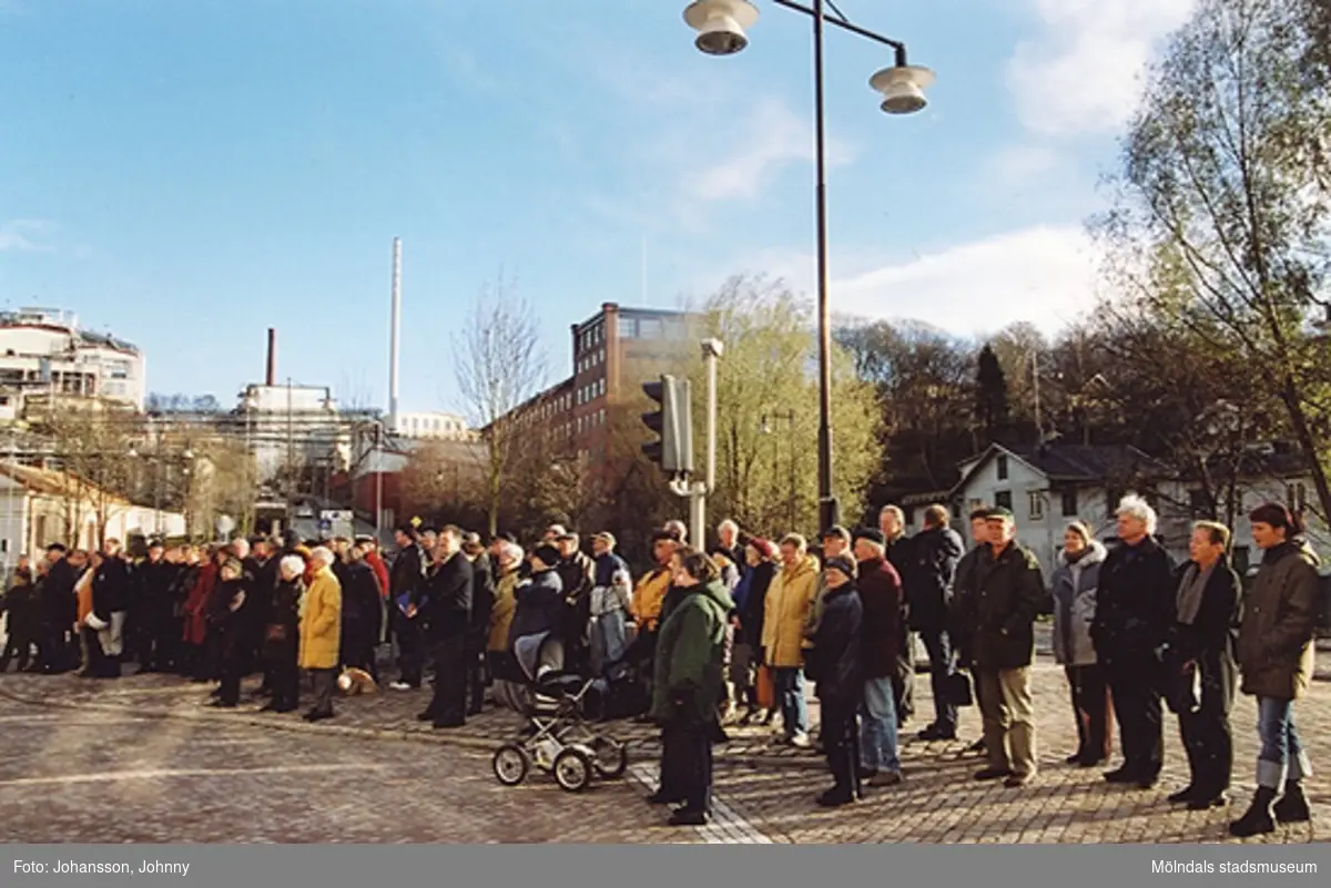 Gamla torget i Mölndal den 22:a november 2001. Folk står och lyssnar till invigningstal efter omläggning och stenläggning av torget. I bakgrunden till vänster ses Soabs fabriker. Till höger ses den höga röda byggnaden Stora Götafors.