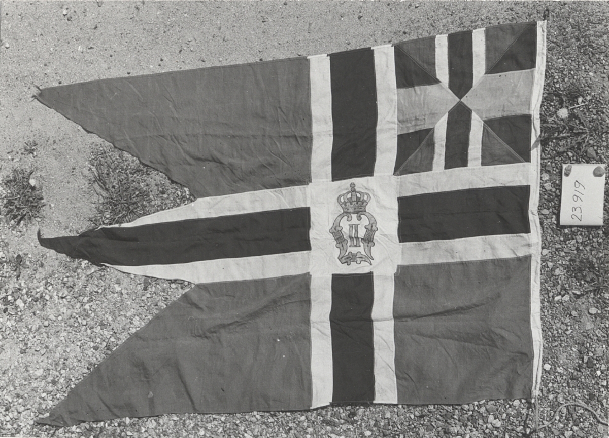 Flagga för Norsk Forenig for Lystseilas.
Yngre unionsmärke med Oscar II:s namn-
chiffer i guld på vit fyrkantbotten i
korsets mitt.Föremålets form: Rektangulär, tretungad