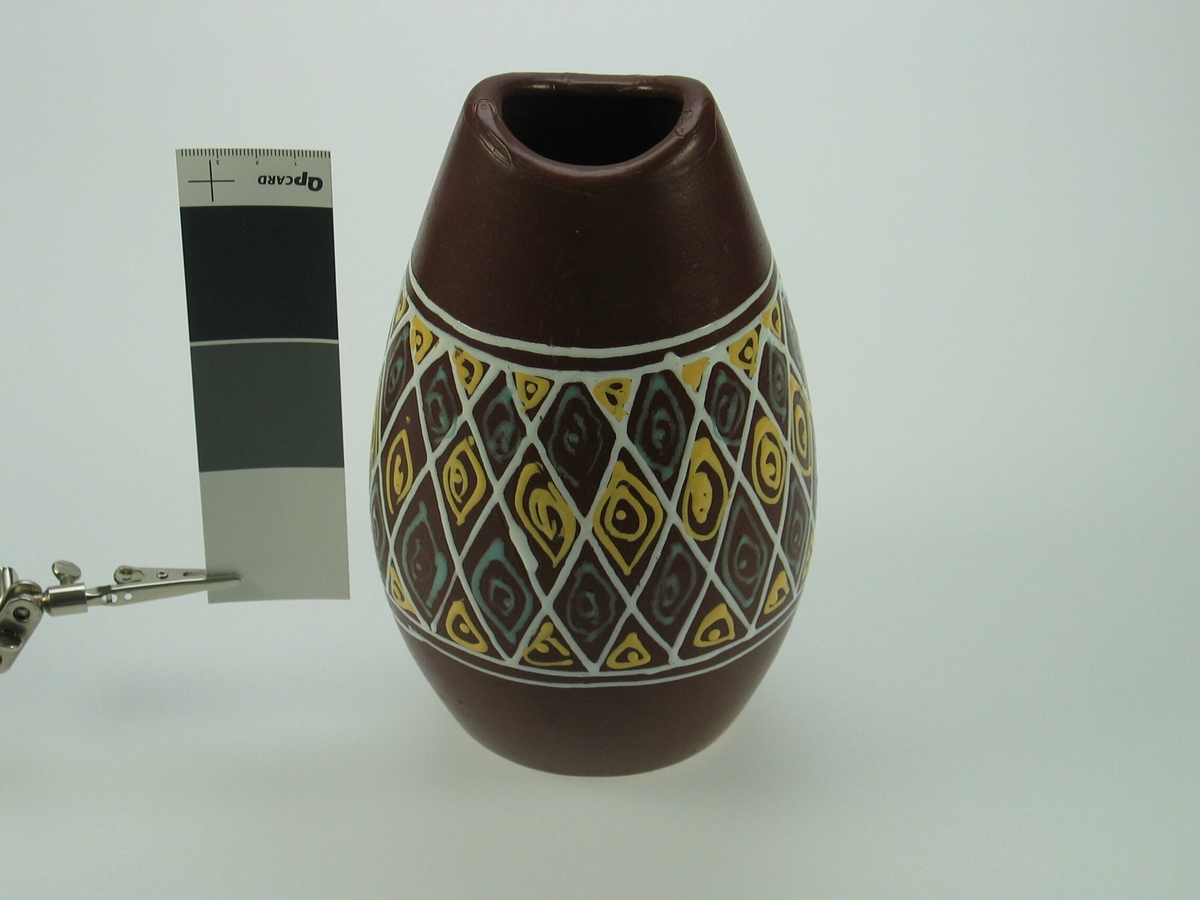 oval vase som blir lit brere i midten. vasen er dekorert med rutemønster i hvit som inneholder grønne og gulr elipser og trekanter .
på undersiden finner man symbolet KK (Kråkerøy keramikk) og nummeret 478. 