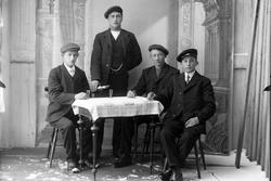 Gruppeortrett av fire unge menn samlet rundt et bord. Én av 