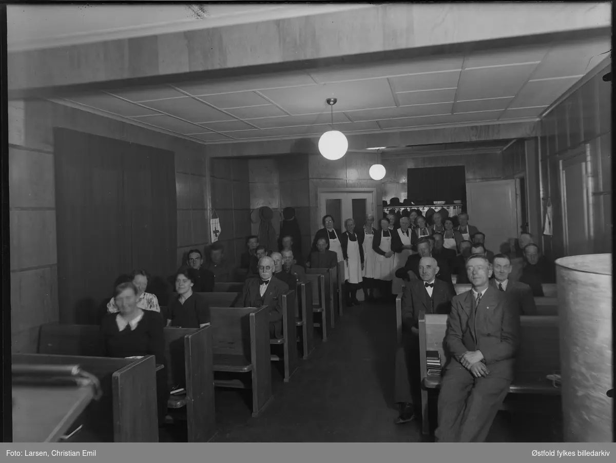 Ukjent gruppe mennesker i forsamlingslokale, serveringspersolanle i bakgrunnen. Ant i Sarpsborg-distriktet 1946. Muligens lille sal i bedehuset, Røde Kors?