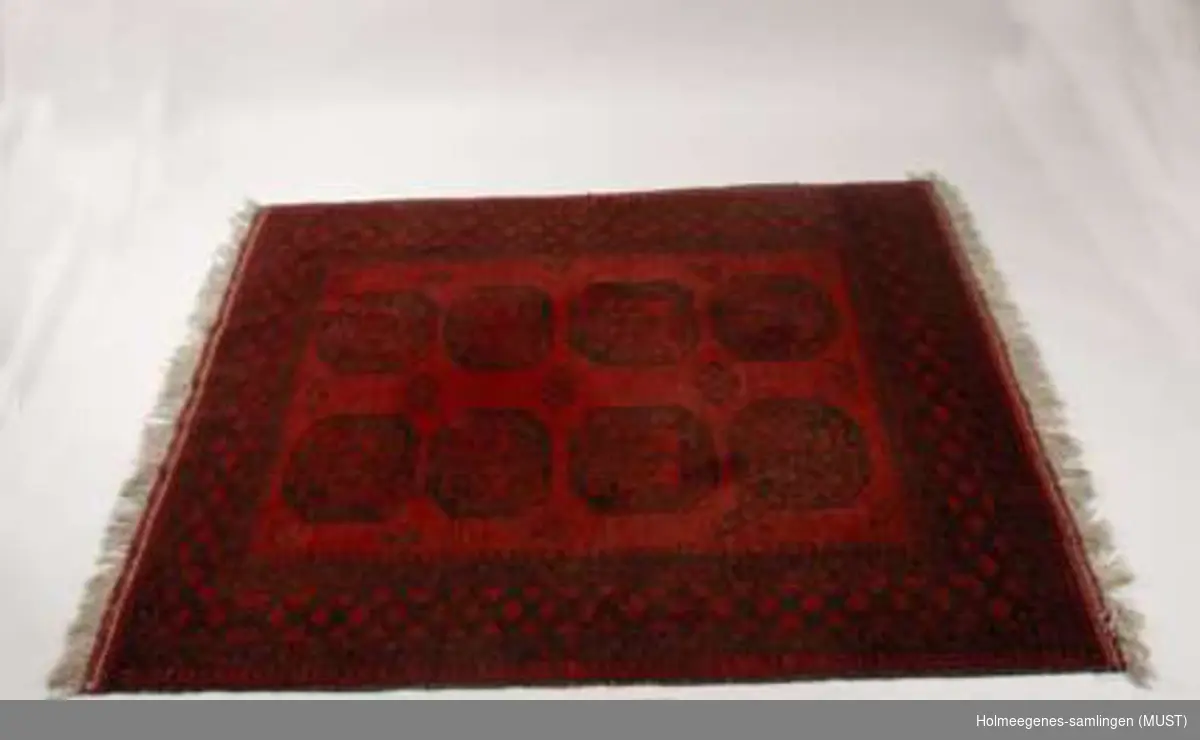 Håndknyttet afghansk teppe i rødt, sort og hvitt som lå under det runde bordet (ST-K.HE.00200) i dagligstuen.