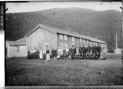 En forsamling av menn, kvinner og barn foran en bygning.