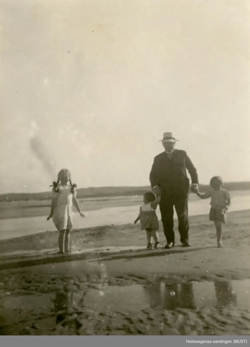 Tre barn og en voksen mann går tur langs en sandstrand.