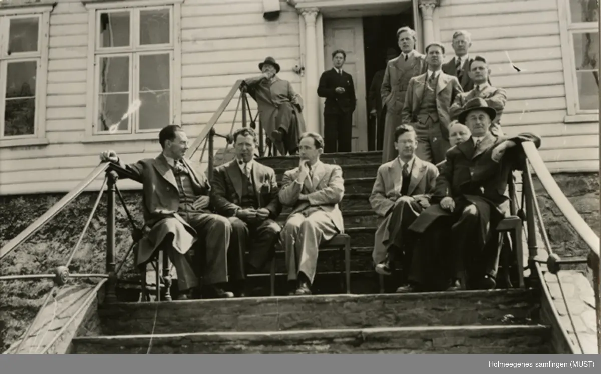 På hovedtrappa på Kongsgård skole. Dresskledte menn sitter på stoler på trappa. Kopiert på postkort-papir.