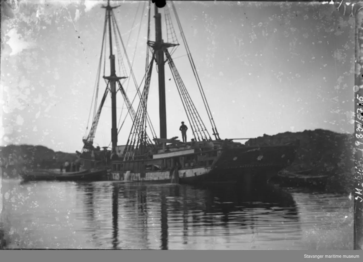 Skonnert "Lizzie Waters" av Sunderland. Muligens havarist, flere menn på dekk, 4 mann i robåt ved skipssiden. Skipet har ankret opp, antagelig på Kvitsøy.