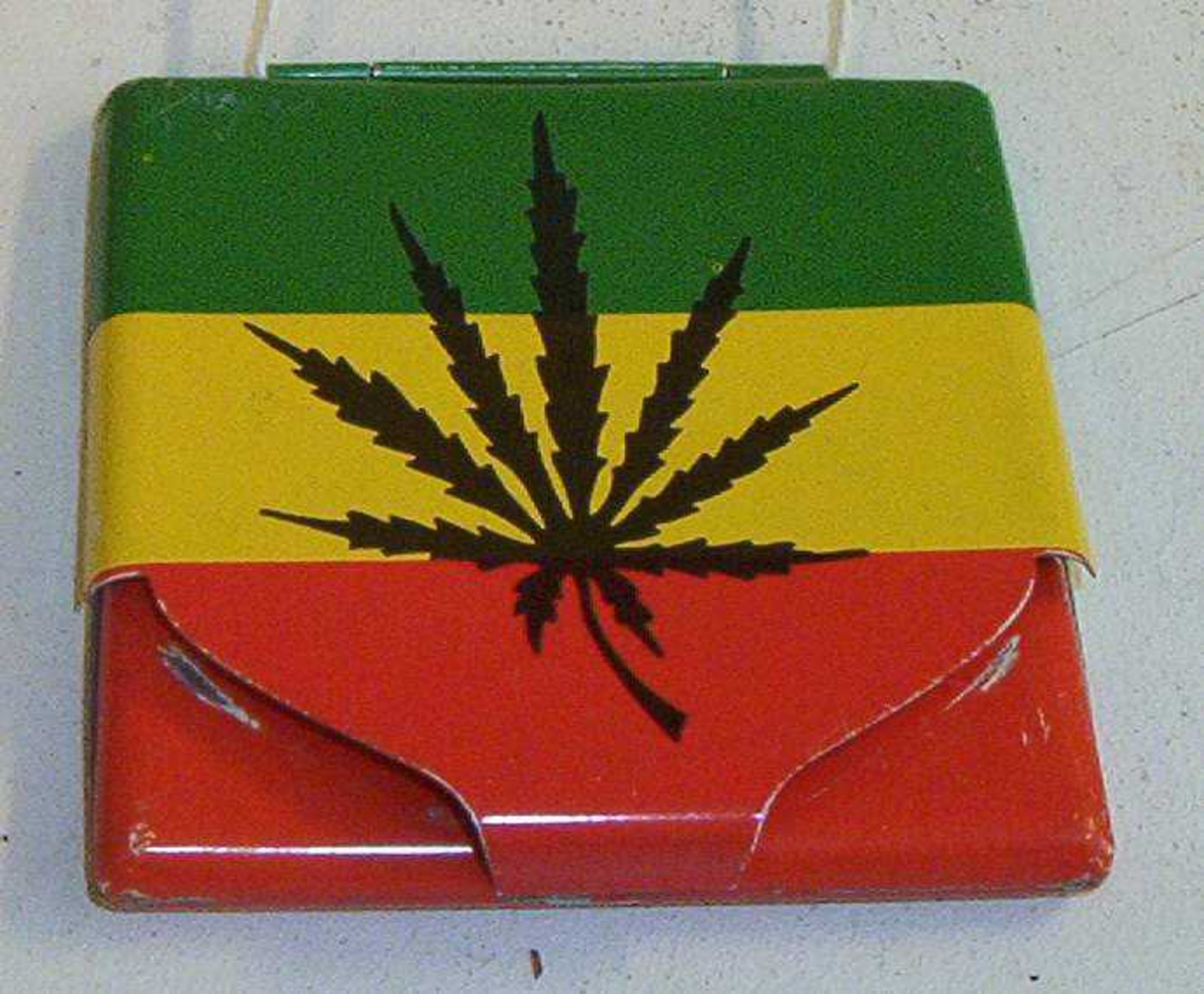 Sigaretteske, sigarettetui. Grønn, gul og rød farget, Jamaica fargene. På den ene siden står det Bob Marley samt et bilde av han, på den andre siden er det bilde av et hasjblad.